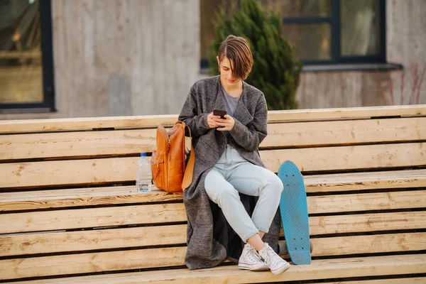 Young woman with a skateboard is resting on a 2 stage bench. lifestyle photo. — Stock Photo, Image