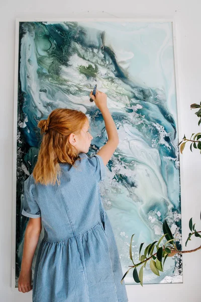 Adolescente pelirroja chica está pintando en un lienzo colgando de la pared . —  Fotos de Stock