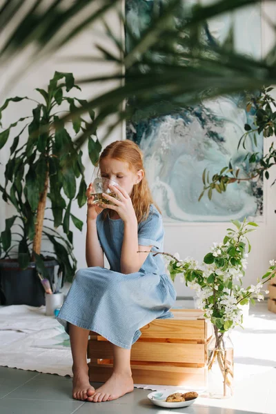 Adolescente pelirroja chica está sentado en una caja, beber té en un taller . —  Fotos de Stock