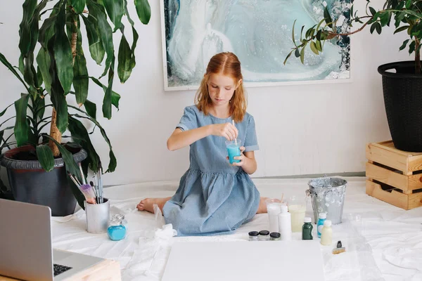 Teenage redhead girl is painting with brush on big canvas on floor in a workshop. — Stock Photo, Image