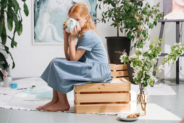 Adolescente rousse est assis sur une boîte, boire du thé dans un atelier . — Photo