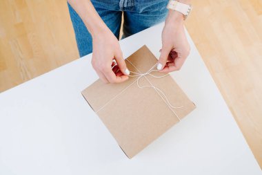 Gündelik kıyafetler giyen kadın posta karton kutu bağlama, evde düğüm yapıyor