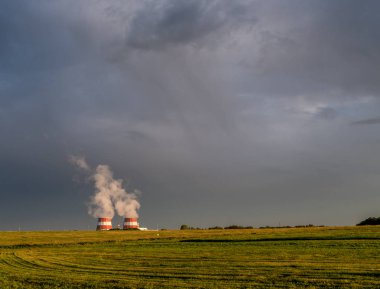 Biçilmiş alan, gri bulutlu gökyüzü ve ufuk üzerinde buharlı soğutma kuleleri