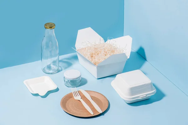 Recyclable paper tableware, cornstarch cutlery, glassware over blue