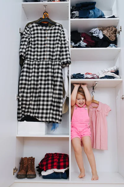 Πορτρέτο του μικρού κοριτσιού σε νέες ροζ φόρμες παίζοντας στο εσωτερικό της ανοιχτής ντουλάπας — Φωτογραφία Αρχείου