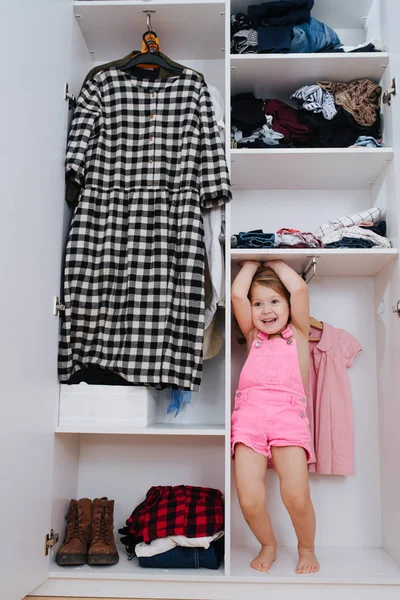 Πορτρέτο του μικρού κοριτσιού σε νέες ροζ φόρμες παίζοντας στο εσωτερικό της ανοιχτής ντουλάπας — Φωτογραφία Αρχείου