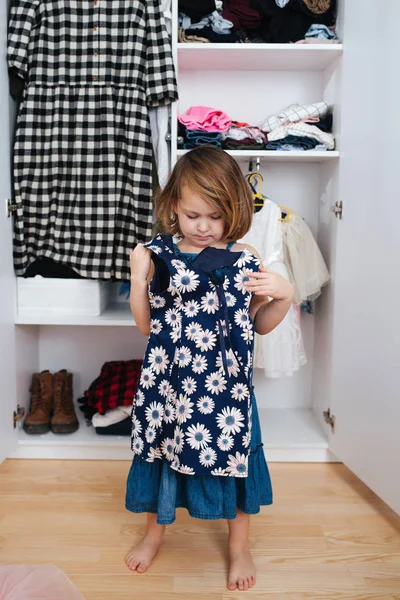 Menina está experimentando em novo vestido na frente do guarda-roupa aberto cheio de roupas — Fotografia de Stock