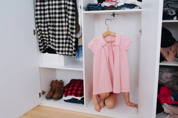 Портрет маленькой девочки в розовом комбинезоне, играющей внутри открытого шкафа — стоковое фото