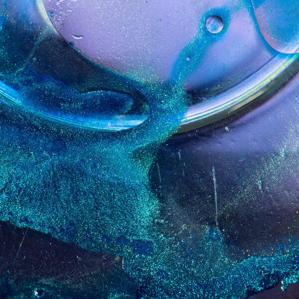 Macro shot suspension of particles in a colored emulsion over backlit background