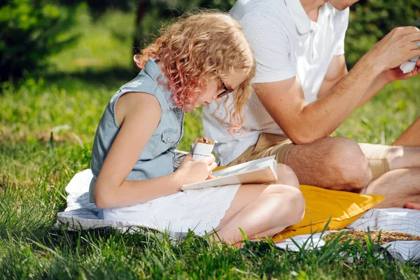 Tiener meisje lezen boek op gras tijdens familie picknick in de tuinen — Stockfoto