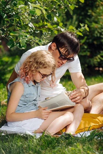 Tiener meisje lezen boek met haar vader op gras tijdens familie picknick — Stockfoto