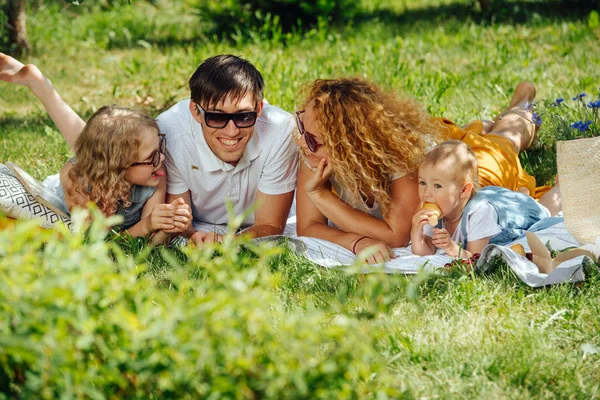 Ağaçların nazik gölgesi altında bahçelerde çim üzerinde aile piknik