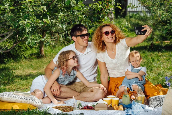Family picnic on grass in the gardens under gentle shade of trees — Stock Photo, Image