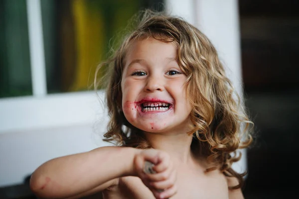 Cute shirtless preschooler girl with mouth dirty in jam grimacing, while eating — Stock Photo, Image