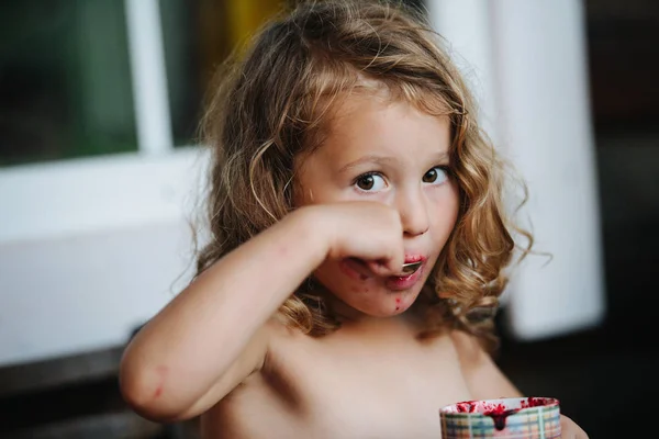 Cute shirtless preschooler girl with mouth dirty in jam grimacing, while eating — Stock Photo, Image