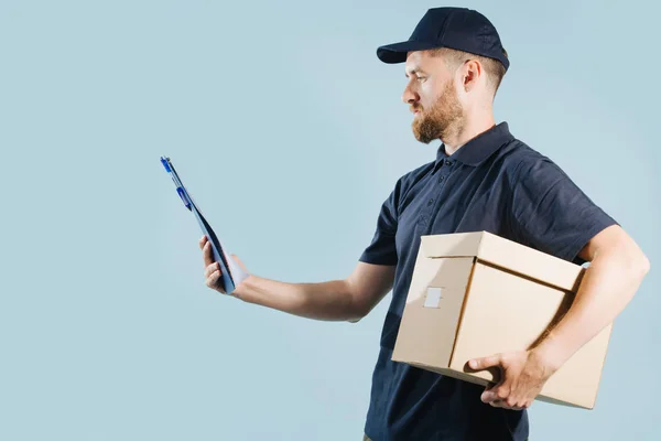 Delivery man in uniform is checking his orders list while holding box under arm