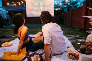 Aşık çift bir film izlerken, alacakaranlıkta, bir avluda çim dışında