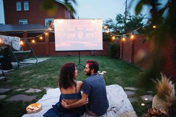 Pareja enamorada viendo una película, en el crepúsculo, afuera en el césped en un patio —  Fotos de Stock
