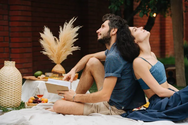 Coppia innamorata sta leggendo libro insieme durante il picnic sul prato nel loro cortile — Foto Stock