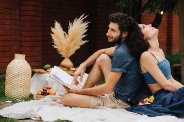 Aşık çift avlusunda çim piknik sırasında birlikte kitap okuyor