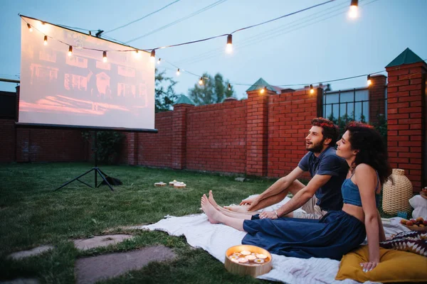 Para w miłości oglądania filmu, w zmierzchu, na zewnątrz na trawniku na dziedzińcu — Zdjęcie stockowe