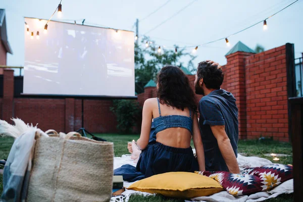 Casal apaixonado assistindo um filme, no crepúsculo, fora no gramado em um pátio — Fotografia de Stock