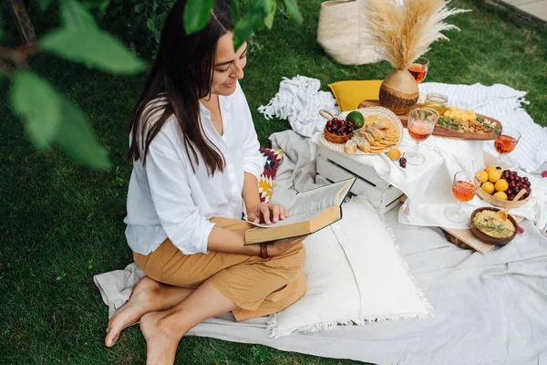 Ung kvinna läser en bok, sitter på benen, på en vit trasa på Picnic — Stockfoto