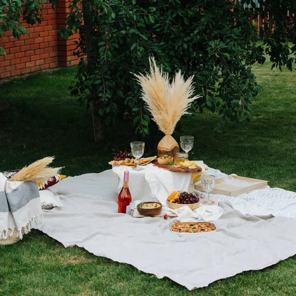 Appetizers table for picnic, full of snack. White cloth spread over lawn