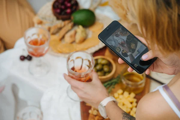 Vrouw het nemen van foto van wijn glas in de hand over een tafel met verschillende hapjes — Stockfoto