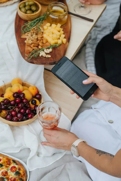 Vrouw leest tekst op haar telefoon over een tafel met verschillende hapjes — Stockfoto