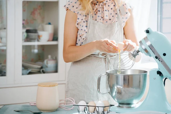 Junge Frau bricht ein Ei in die Schüssel der Küchenmaschine, um einen Teig zu machen — Stockfoto