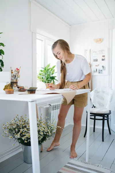 Joven artista dibujo en hoja, detrás de la mesa en casa . — Foto de Stock