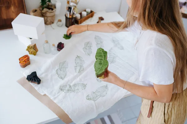 Mujer joven haciendo estampados verdes en forma de hoja en tela con sello de madera . —  Fotos de Stock