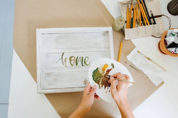Mani femminili che disegnano lettere con vernice su un vassoio di legno bianco Immagine Stock