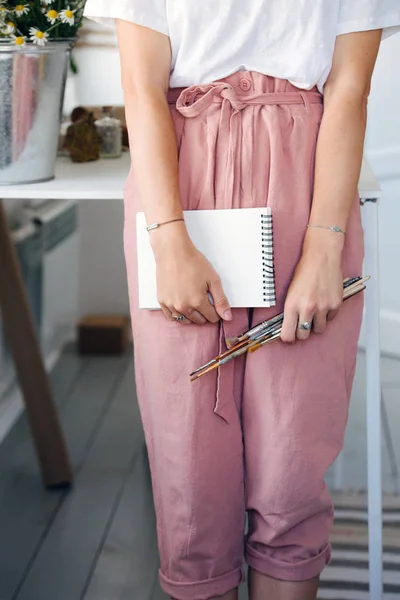 Joven mujer modesta sosteniendo cuaderno de papel y pinceles en sus manos —  Fotos de Stock