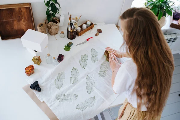 Jeune femme faisant des impressions vertes en forme de feuille sur tissu avec timbre en bois . — Photo