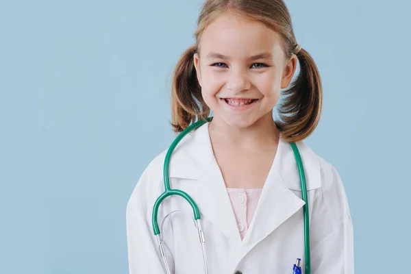 Gülümseyen küçük kız doktor oynuyor, stetoskop ile beyaz cüppe giyiyor — Stok fotoğraf
