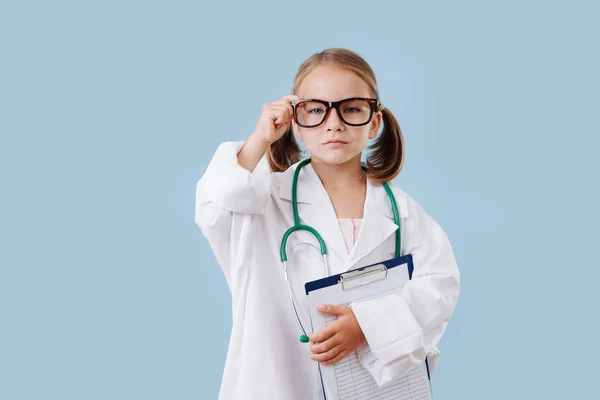 Mosolyogva kislány játszik orvos, fárasztó, hosszú, fehér ruhát sztetoszkóppal — Stock Fotó