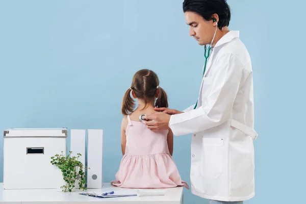 Férfi orvos vizsgálja a gyermek lány, hogy ül egy asztalnál a kórházban — Stock Fotó