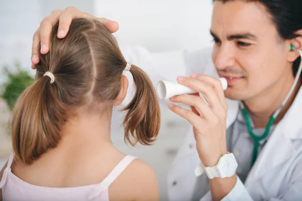 Médico masculino examinando la oreja de una niña en el hospital, usando linterna — Foto de Stock