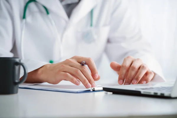 Médico varón que trabaja con el ordenador portátil detrás del escritorio, escribiendo en el papeleo en un hospital . — Foto de Stock