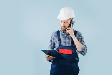 Beyaz kask ve bir telefon ile mavi tulum conserned inşaat işçisi