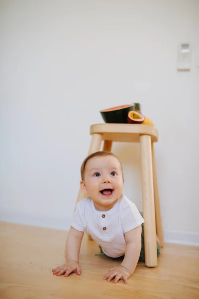 An infant baby is crawling from under the stool with fruits on it — Stock Photo, Image