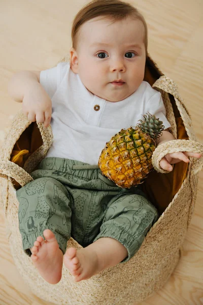 Infant baby with pineapple in a wicker, basket like bag — Stock Photo, Image