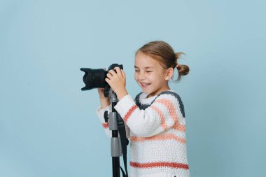 Little girl laughs with eyes closed, about to take photo with camera on tripod clipart
