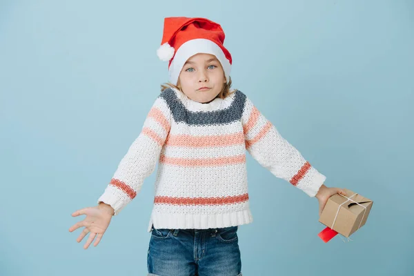 Porträt eines süßen kleinen Erstklässlers mit Weihnachtsmannhut, der mit den Schultern zuckt — Stockfoto
