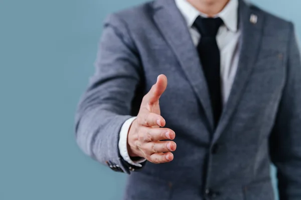 Empresario en traje extendiendo la mano, listo para el apretón de manos sobre fondo azul — Foto de Stock