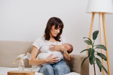 Caucasian mother is decently breastfeeding her baby, without exposing herself. clipart