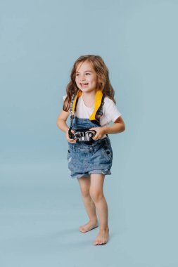 Mutlu küçük kız mavi arka plan üzerinde bir vintage aynalı kamera tutan.