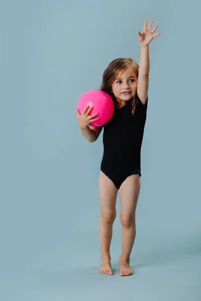 Petite fille dans un justaucorps noir avec boule de gymnastique rose sur fond bleu — Photo